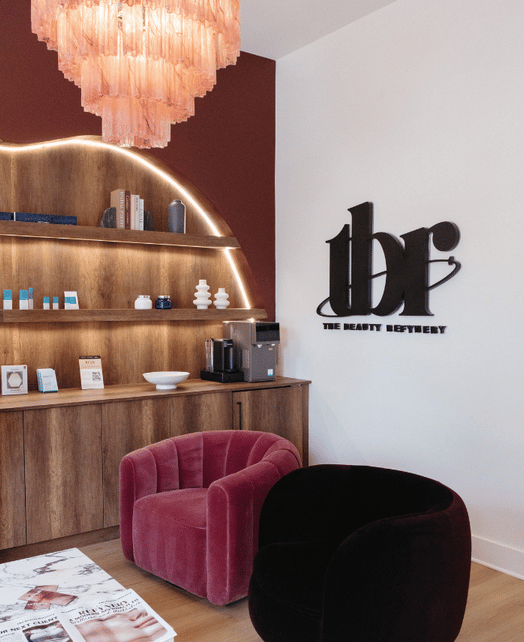 The Beauty Refinery interior with branded wall logo, wooden shelving, and velvet chairs