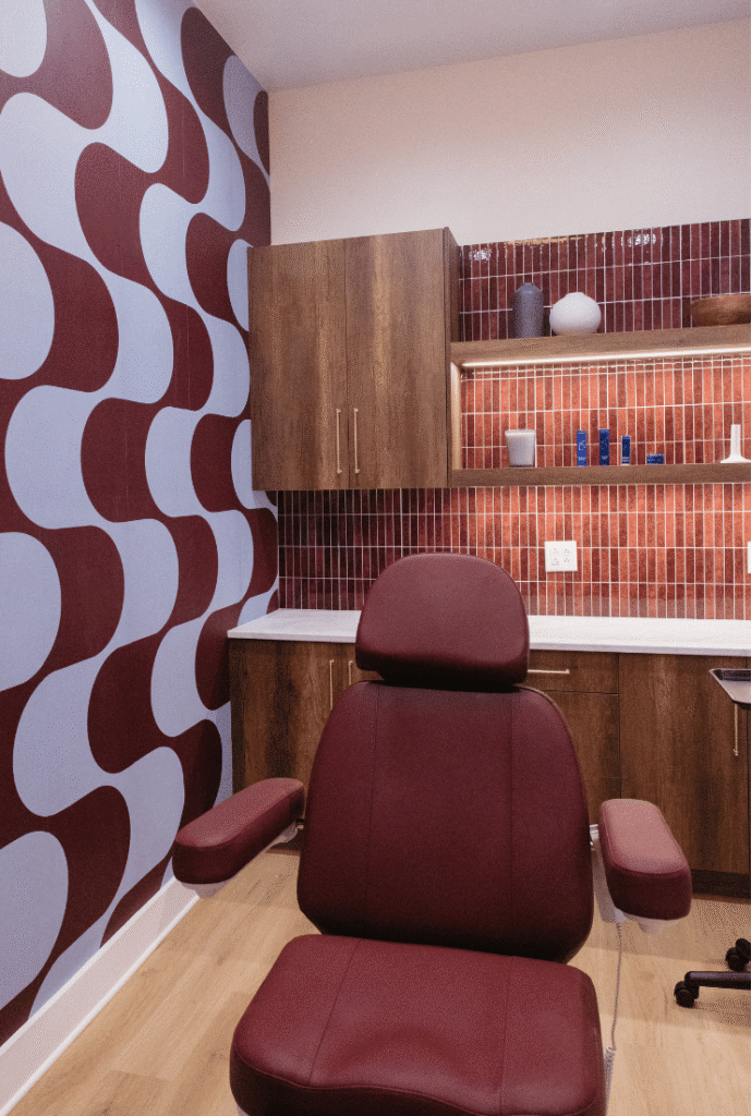 Modern aesthetic treatment room with burgundy treatment chair and wood cabinetry